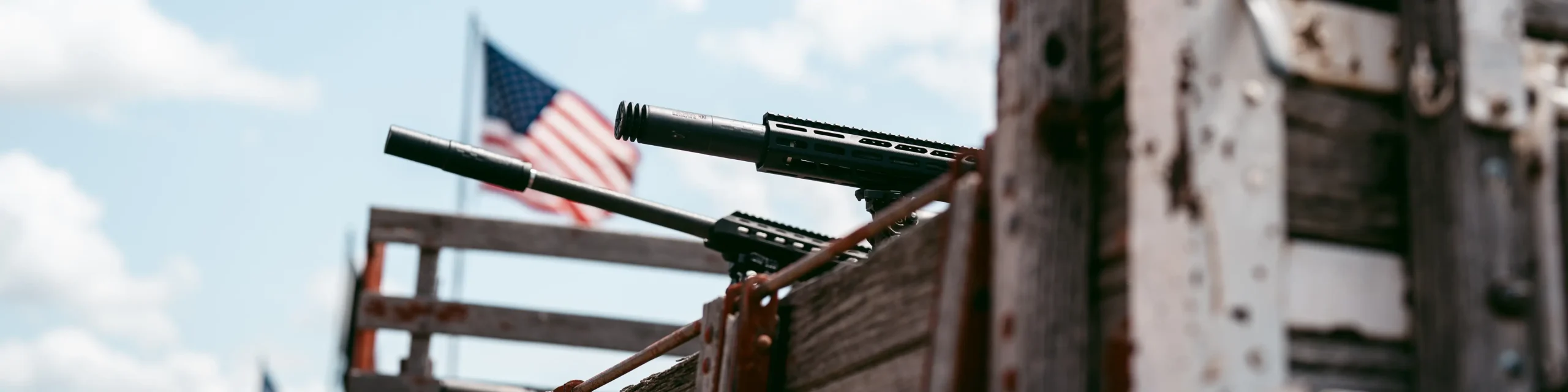 suppressors shooting over a wooden beam with an american flag in the background