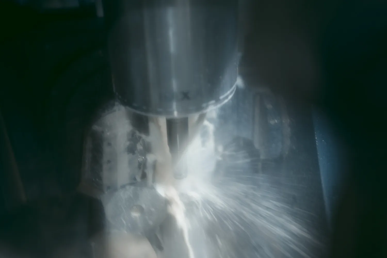 A vertical tombstone-style mill in action. As coolant sprays across the part, the machine cuts one face of the fixture before rotating to the next.