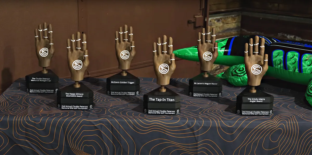 Six SilencerCo Chubbs Peterson trophies on a table. They are shaped like wooden hands with glue marks showing where his hand broke when it was run over by a semi. Each trophy has a SilencerCo logo on it.