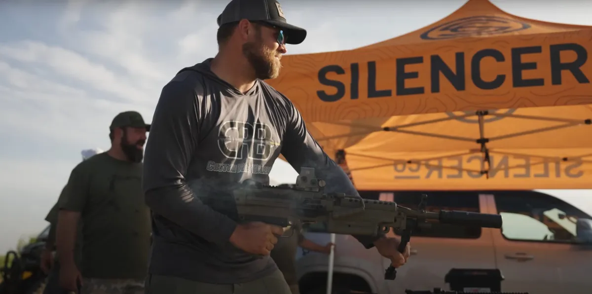 SilencerCo tent in background, man shooting FN M249 belt-fed machine gun in .200 BLK, suppressed with Velos 762 thats mounted with the Charlie ASR Mount