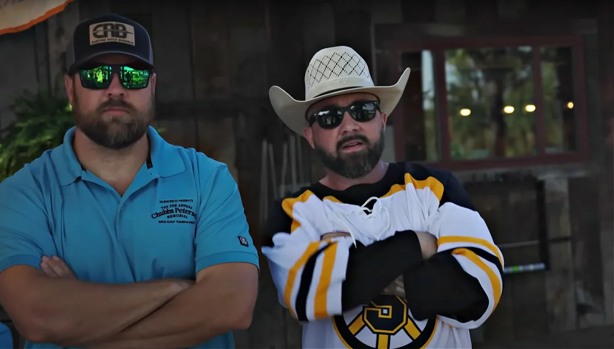 two men standing with arms folded. Man to the right has a Happy Gilmore jersey on.
