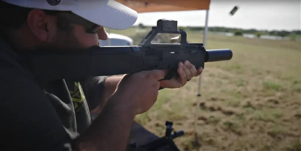 Man shooting the ZEV FDP 9mm machine gun, suppressed with Omaga 9K (1/-28 piston, Alpha piston spring retainer). Full auto, two spent casings flying through the air after exiting the ejection port.