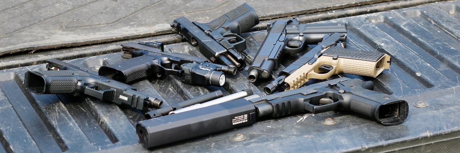 several 9mm handguns on a truckbed, exposing threaded barrels for suppressing a 9mm handgun
